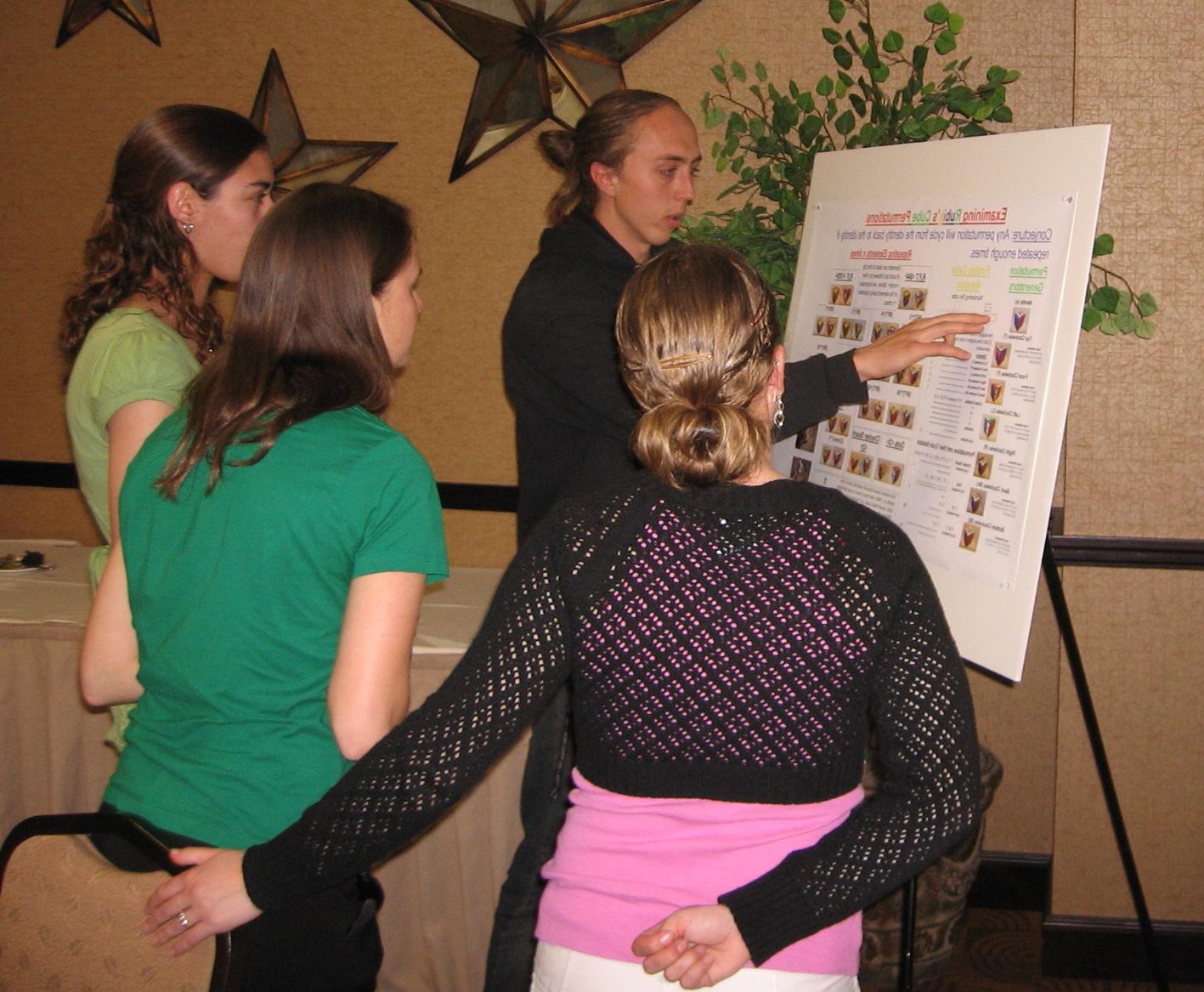 Student gives a presentation from a poster board while a small group watches