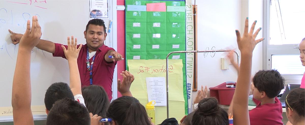 Teacher in an elementary classroom pointing to a student with their hand raised.