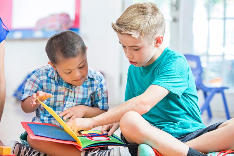 Image of two young childrer interracting with a book together in a brightly lit classroom.