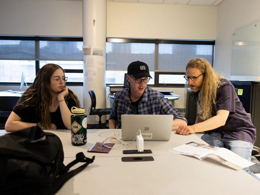 Professor Bergman works with students on a Macbook pro.